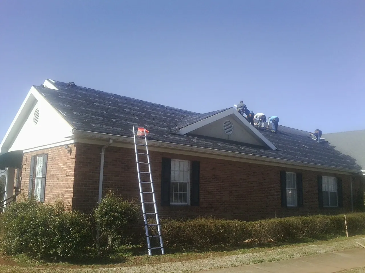 Crew tearing shingles off a brick ranch roof with a ladder set — Metal Roof Repair work by our crew in Pendleton
